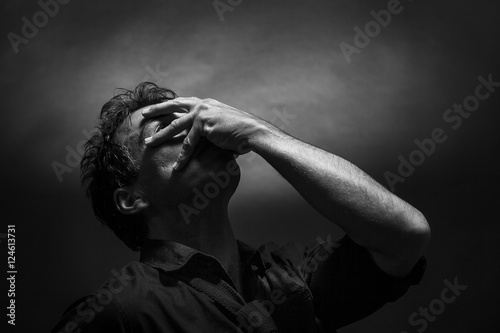 Despairing man low key black and white portrait. Hand over the face