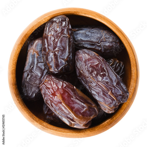 Dried Medjool dates from Morocco in a wooden bowl on white background, also called Mejhool. Large, sweet and succulent fruits of date palms, Phoenix dactylifera. Isolated macro food photo close up.