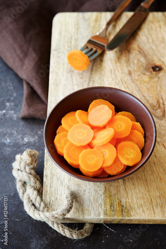 Cooked carrots in the cup on brown wooden background