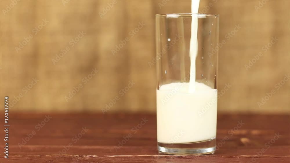 Milk pouring into glass on a wooden table and brown background Milk pouring into glass on a wooden table and brown background