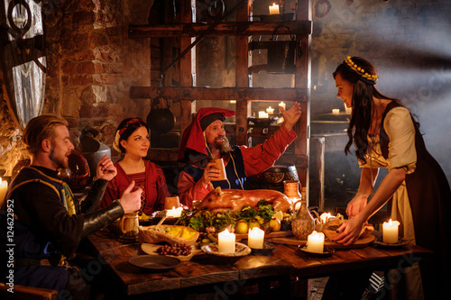 Fotografie, Obraz Medieval people eat and drink in ancient castle kitchen interior