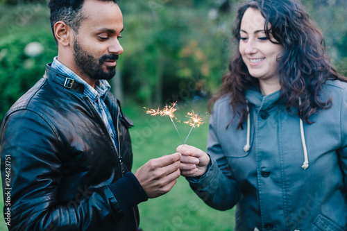 Young couple in love celebrating an event, New Year is coming, they are holding three lit sparkler behind them forest © loreanto