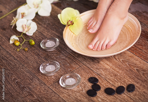 Female feet with drops of water in spa bowl with water and flowers