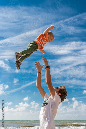 The elder brother throws his younger  on the beach against the backdrop of the sea. Happy carefree childhood