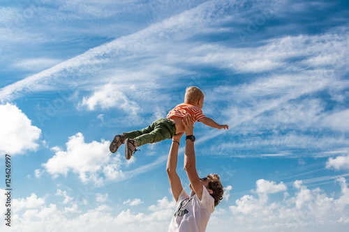 The elder brother throws his younger  on the beach against the backdrop of the sea. Happy carefree childhood
