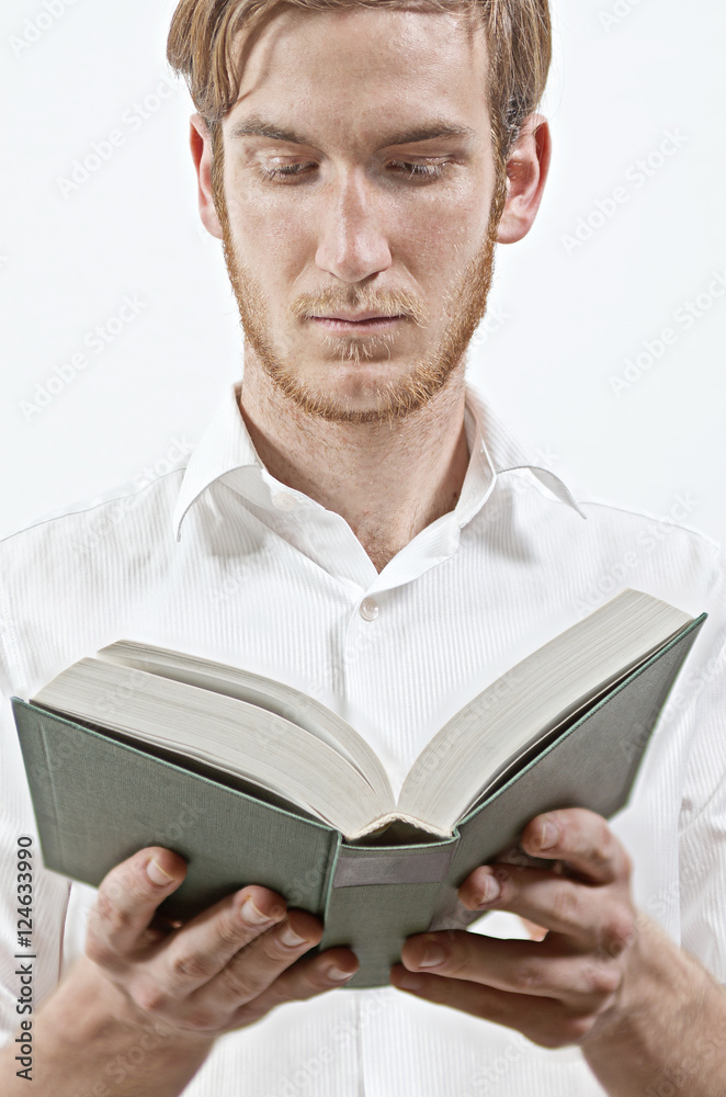 Standing Young Adult Man in White Shirt Holds a Book in His Hands, Reading Standing Young Adult Man in White Shirt Holds a Book in His Hands, Reading