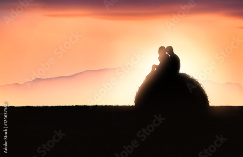 Silhouette di una giovane coppia sopra una balla di fieno al tramonto photo