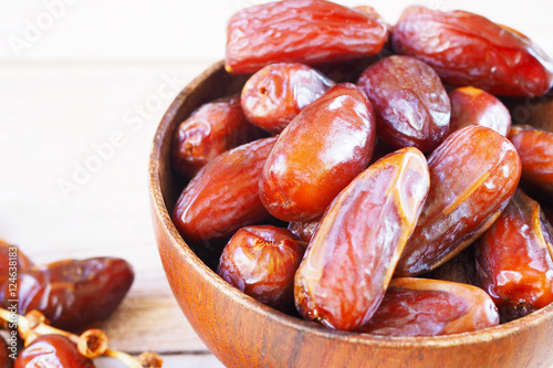 Close up of a bowl of dried dates on a wooden background.