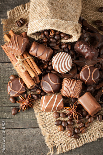 Assortment of dark, white and milk chocolate stack, chips. Chocolate and coffee beans on rustic wooden sacking background. Spices, cinnamon. Selective macro focus. Chocolates background. Sweets