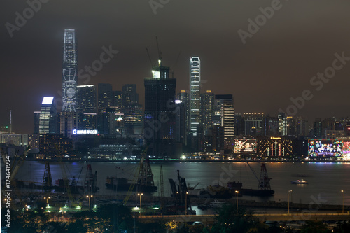 Waterside view of Hong Kong with illuminated skyscrapers at night, industrial ships at anchor in foreground