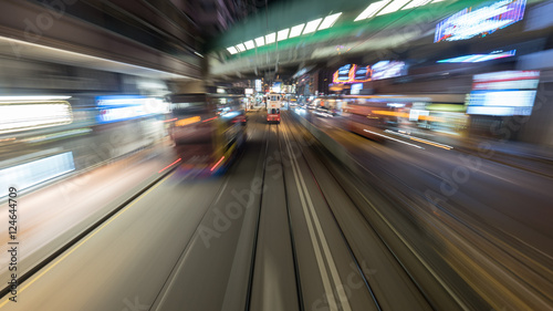 Traveling through night Hong Kong by double-decker tram. View to road with moving bus and rails with another tram. Shot in motion