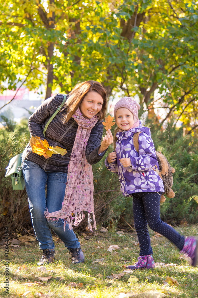 Fototapeta premium Young woman and her little daughter shows autumn leaves