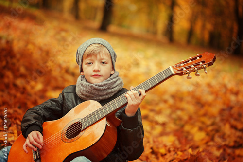 Little boy playing guitar on nature background, autumn day. Children's interest in music .