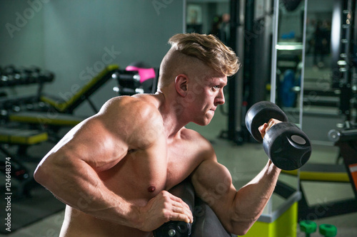 Athletic strong bodybuilder deals with a dumbbell in the gym