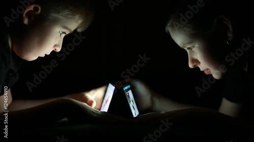  children look to smartphones in the dark on black background