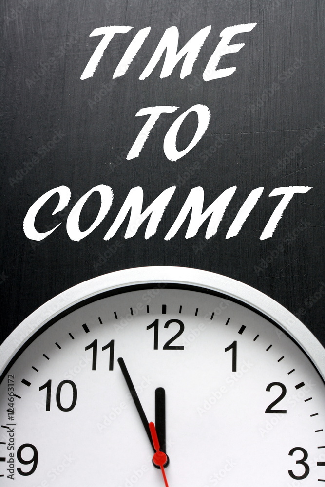 The words Time To Commit on a blackboard above a clock as a call to action when making decisions The words Time To Commit on a blackboard above a clock as a call to action when making decisions