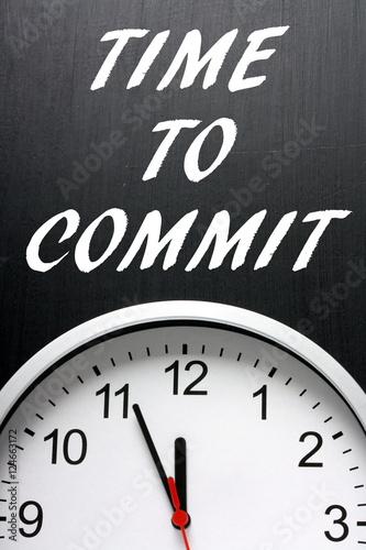The words Time To Commit on a blackboard above a clock as a call to action when making decisions