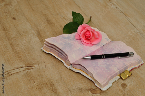 Fototapeta Naklejka Na Ścianę i Meble -  An open diary on a wooden table with a pink rose, pen and a mug