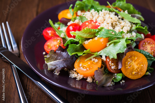 Fresh healthy salad with quinoa, cherry tomatoes and mixed greens (arugula, mesclun, mache) on wood background close up. Food and health. Superfood meal.