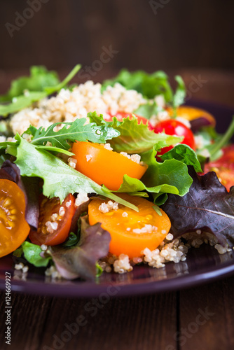 Fresh healthy salad with quinoa, cherry tomatoes and mixed greens (arugula, mesclun, mache) on wood background close up. Food and health. Superfood meal.