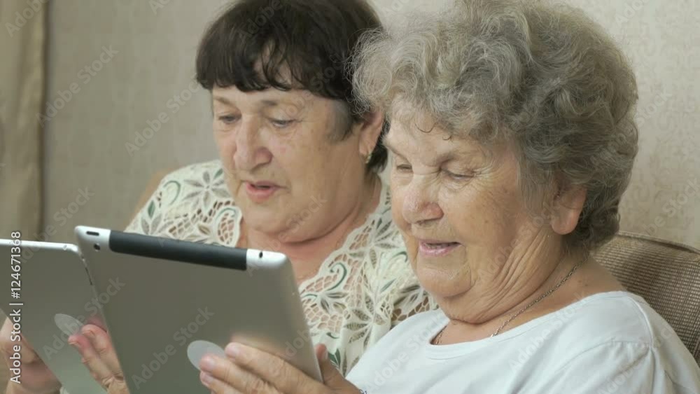 Two elderly sisters holding silver digital tablets Two elderly sisters holding silver digital tablets