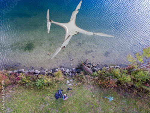 Luftbild See - Mann am Ufer lenkt Flugdrohne mit Fernsteuerung photo