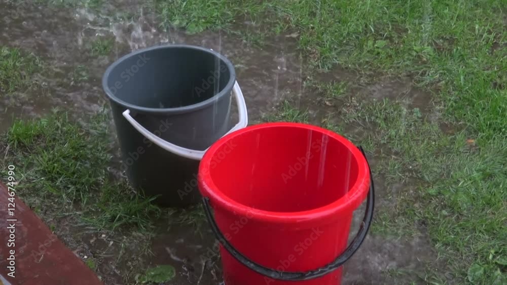 Rain falling in plastic buckets standing on lawn during summer storm Rain falling in plastic buckets standing on lawn during summer storm