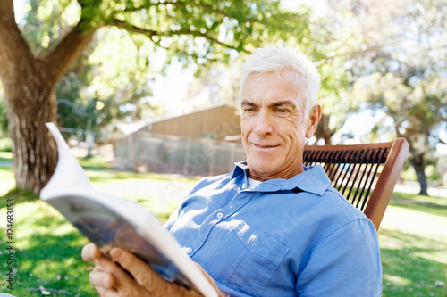 Senior man sittingin park while reading book photo