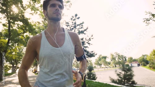 Great active young man jogging on park, while listening to music in earphones from mp3 player smartphone. photo