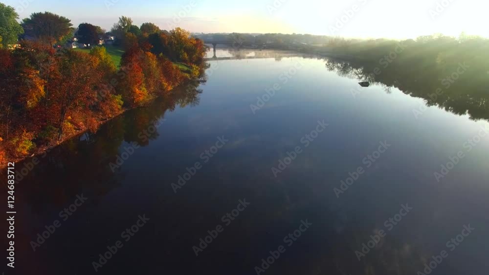 Scenic flight over foggy river with Autumn colors and sunbeams.
