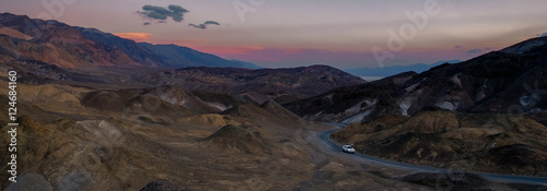 Automobile (SUV) driving on a winding desert road through rugged terrain at twilight