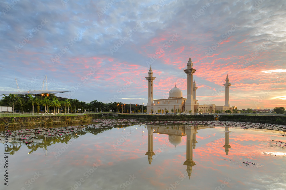 Naklejka premium View and reflection of Bukit Jelutong Mosque with stunning blue and red clouds and ray of lights during sunrise.