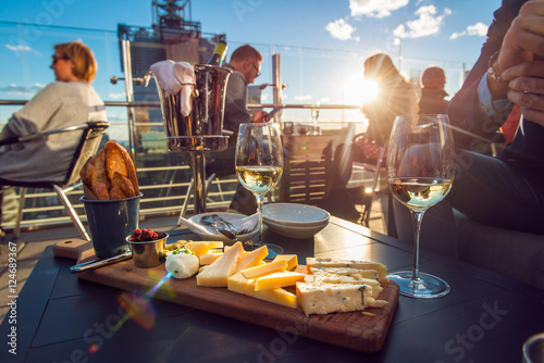 People having dinner at rooftop restaurant with wine and cheese at sunset time. photo