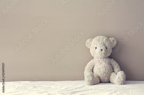 Fototapeta vintage teddy bear sit on the right side white bed at headboard