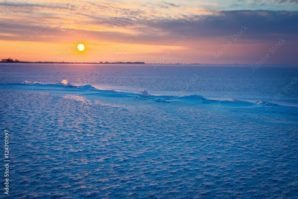 Winter landscape with frozen lake, cracks and sunset sky.