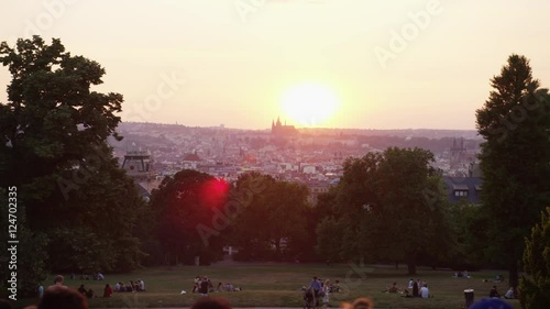 A moving shot behind a crowd of tourists hanging out in Riegrovy Sady park with a view of Prague castle during sunset.  Smoke hang sin the air. 4k. Slow motion. photo