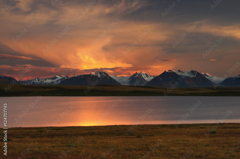 Highland dawn sunset lake on a background of snow ice covered high mountains and glaciers under cloudy colorful light illuminated dramatic sky, Plateau Ukok, Altai Siberia, Russia