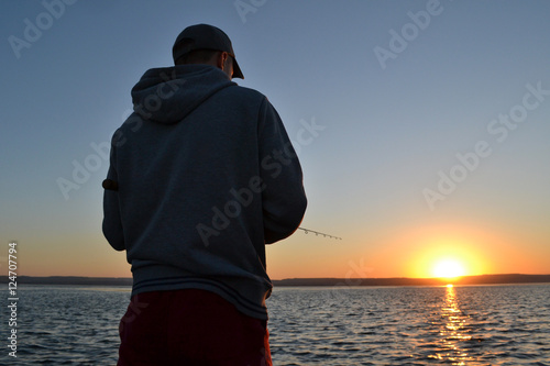 Fisherman with spinning on the evening dawn. The sun goes below the horizon.