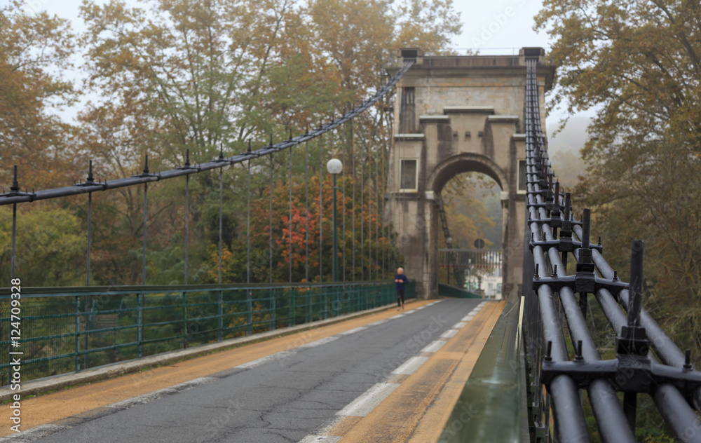 Fototapeta premium Man running over an old suspension bridge during a foggy, autumn day.