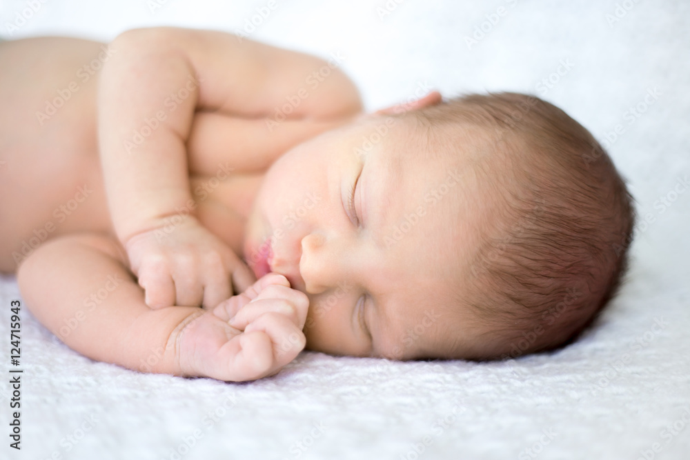 Close-up portrait of sweet newborn infant sleeping quietly on bed on white blanket with little hands lying near mouth Close-up portrait of sweet newborn infant sleeping quietly on bed on white blanket with little hands lying near mouth