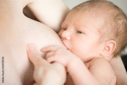 Close-up portrait of sweet newborn baby breastfeeding. Young mother holding her baby on her arms feeding. Happy motherhood concept, indoors shot