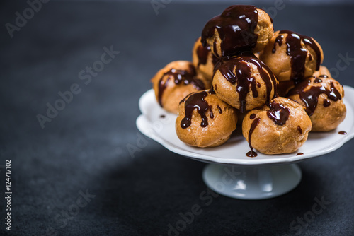 Tableau sur toile Stack of profiteroles eclairs with dark melted chocolate