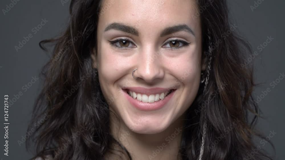 CLose up smiling face of a beautiful young woman with piercings, gray background