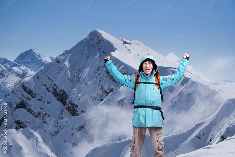 Happy male mountain climber with arms raised above the head. In the background the high mountains.