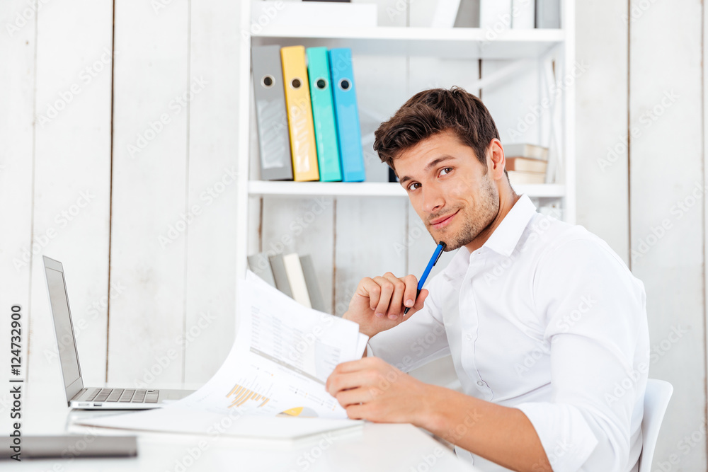 Smiling young businessman signing documents and looking at camera Smiling young businessman signing documents and looking at camera
