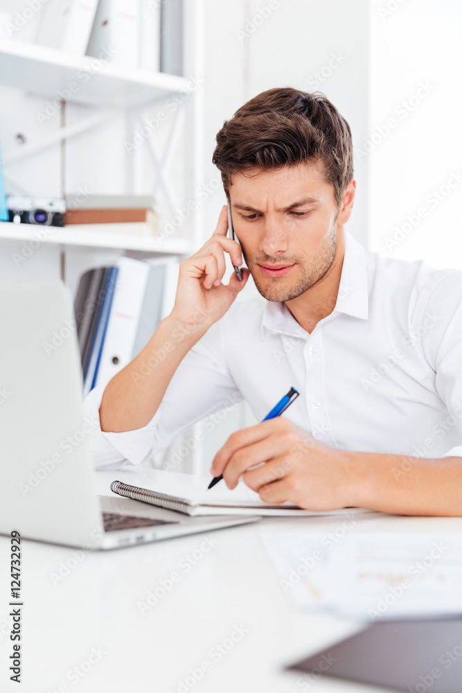 Businessman talking on the mobile phone and making notes Businessman talking on the mobile phone and making notes