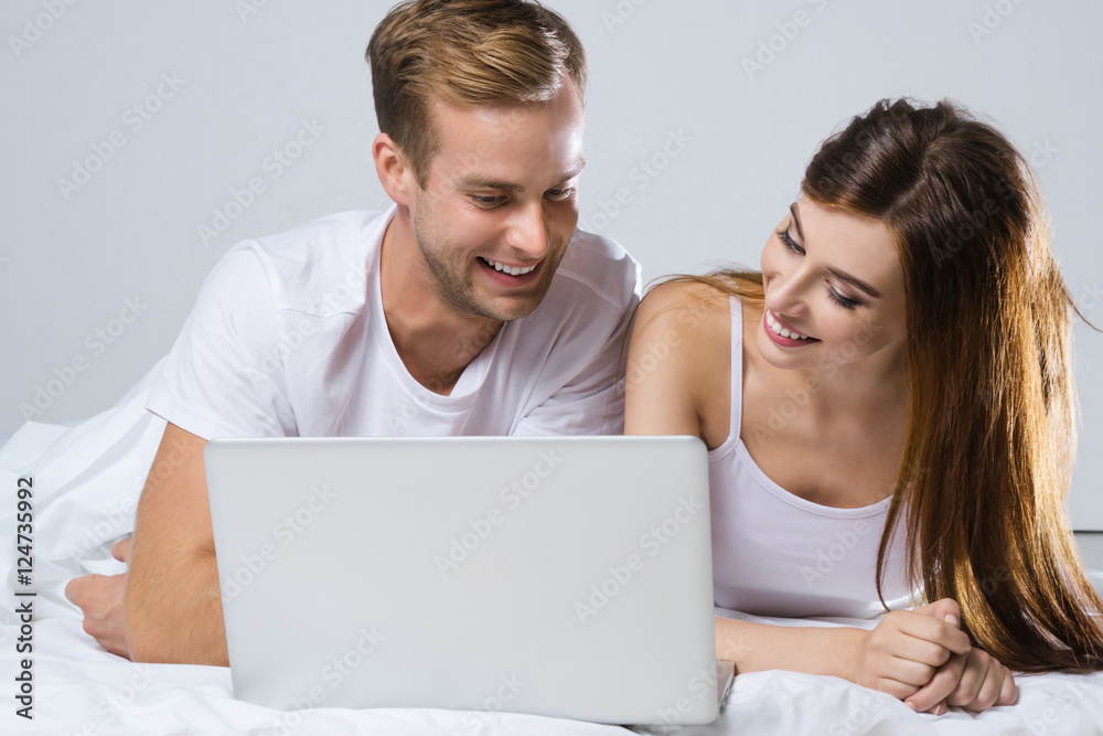 Couple using laptop, on bed
