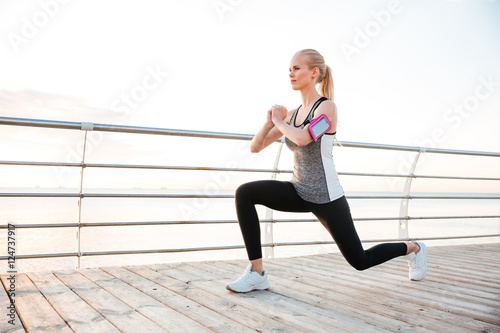 Attractive young sportswoman stretching legs on pier