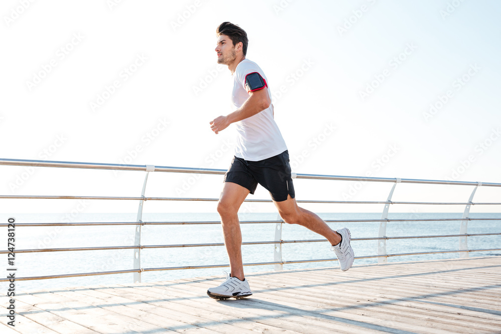 Confident young man athlete running on pier in the morning
