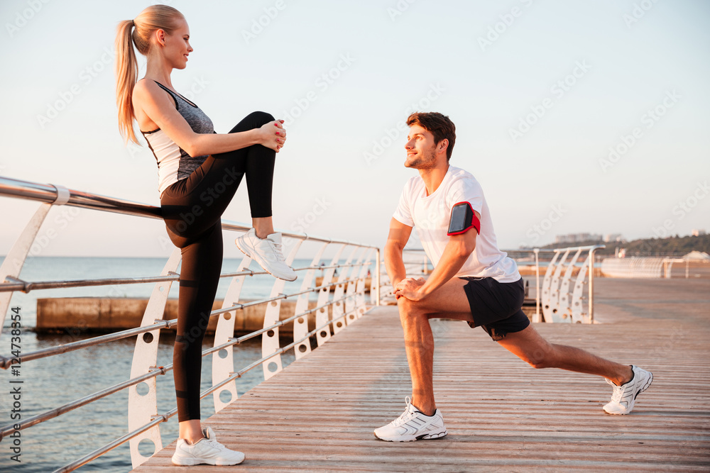 Young man and woman stretching legs at sunrise